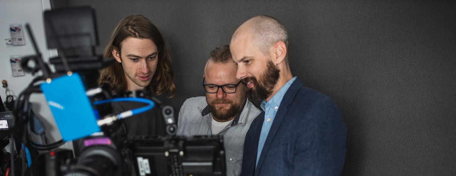 Three men behind camera equipment