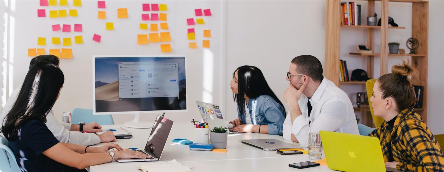 A group of office workers gather around a monitor in a meeting