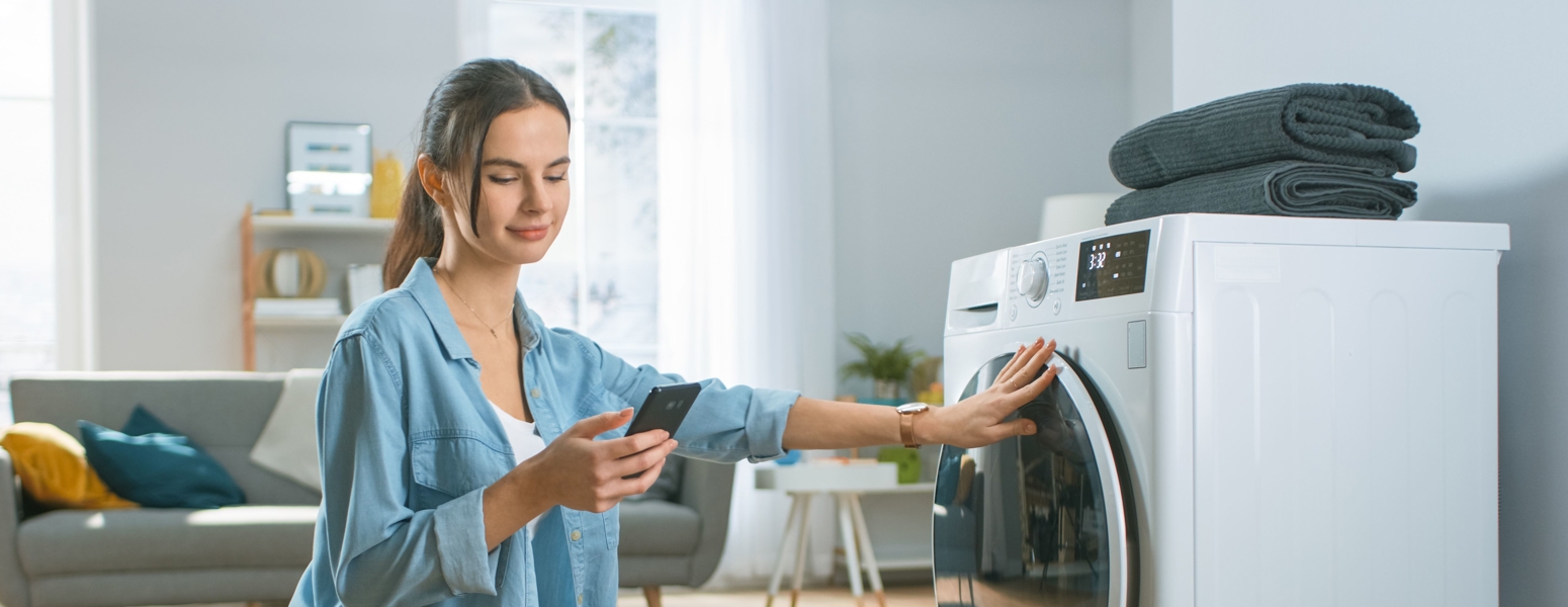 A woman looking at her phone next to a washing machne