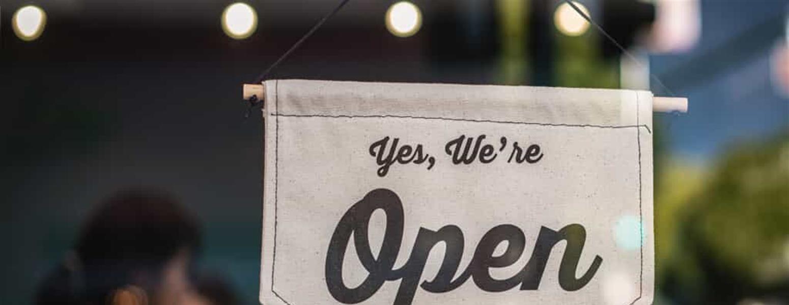 Two people celebrate behind a store open sign