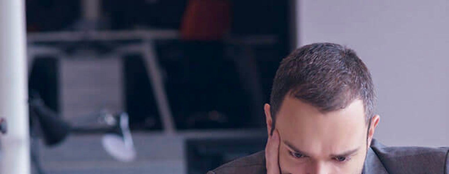 Man sitting in front of a laptop with is hand on his face