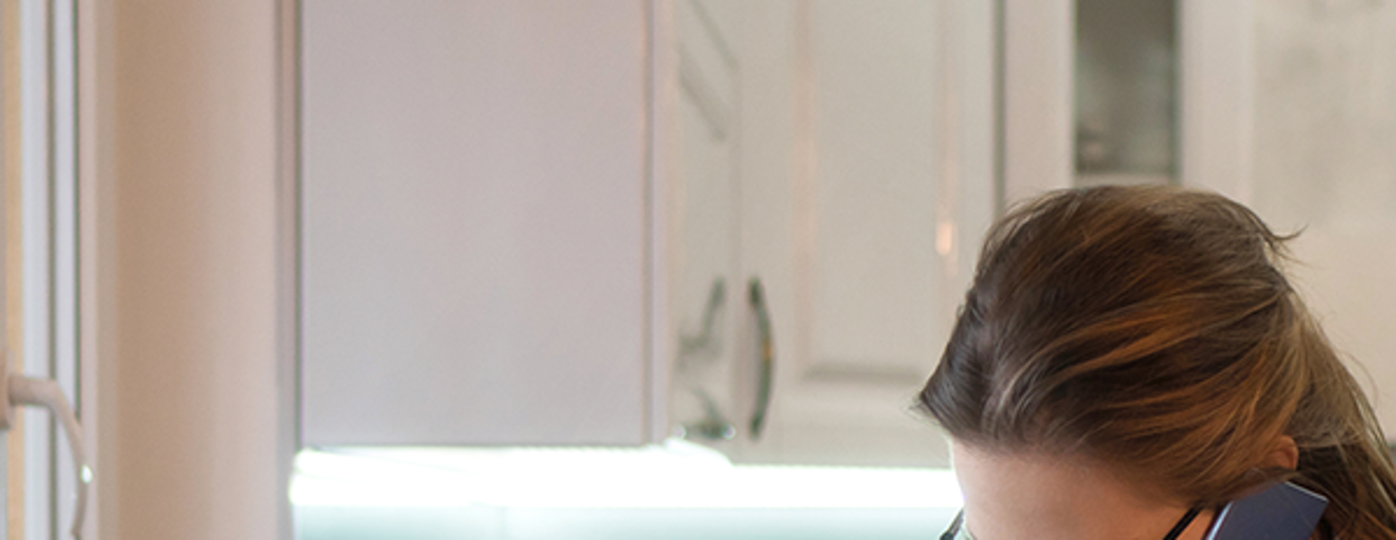 Woman in her kitchen on the phone in front of her laptop