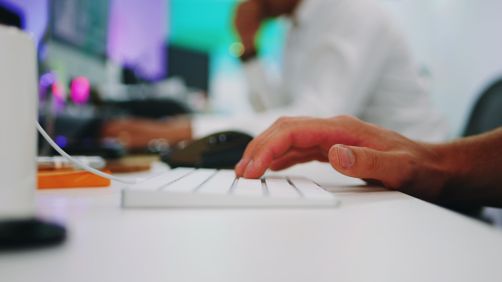 A person types on a keyboard in front of a computer monitor 