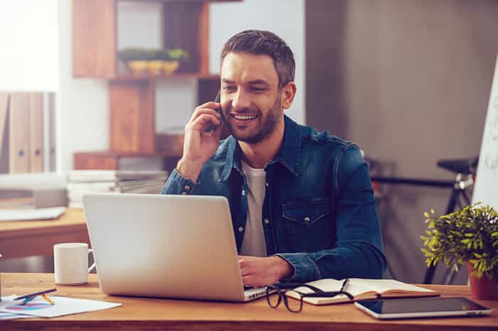 A man on his laptop and talking on his cell phone.