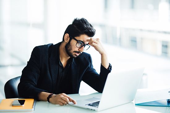 Man sits at a laptop computer looking frustrated.