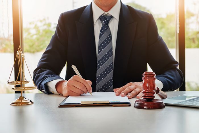 attorney signing a document with scales and a gavel sitting on his desk