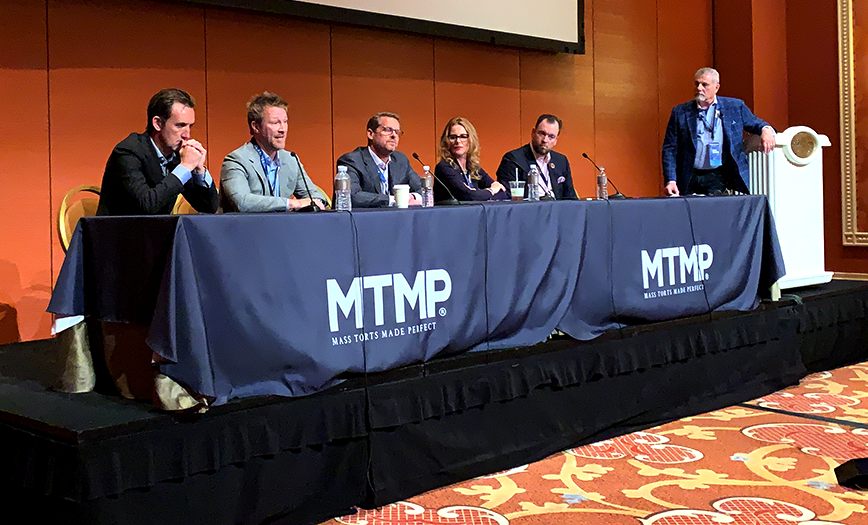 A panel of digital marketing experts sits at a table onstage in front of microphones, addressing the crowd at Mass Torts Made Perfect (MTMP).