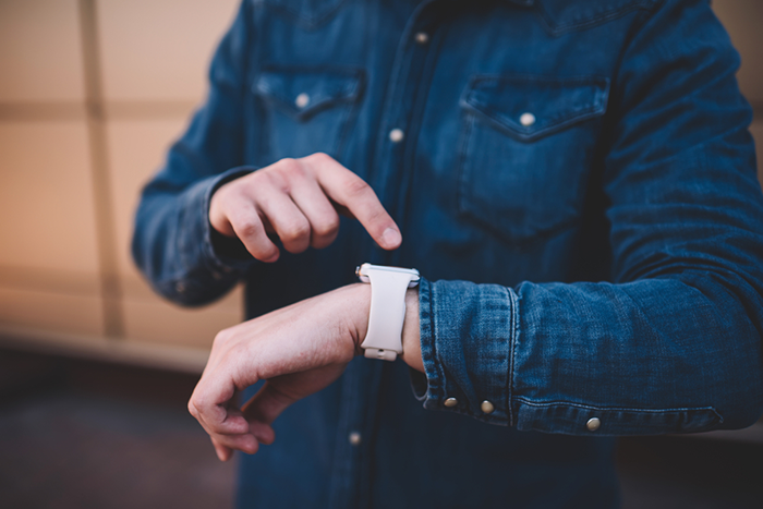 man in denim shirt using his smart watch