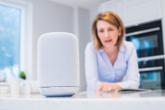 Woman standing at kitchen counter, speaking into a smart speaker