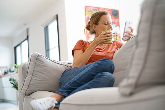 A woman looking on her phone while sitting on her couch at home.